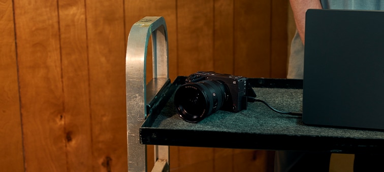 Εικόνα χρήσης φωτογραφικής μηχανής FX5 με τυπικό φακό ακουμπισμένο σε τροχήλατο με επένδυση δίπλα σε laptop.
